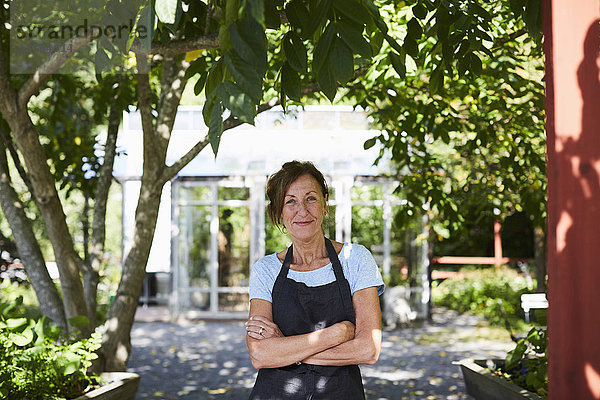 Porträt einer selbstbewussten Gärtnerin mit gekreuzten Armen auf dem Hof