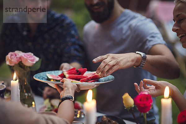 Abgeschnittenes Bild einer Frau  die Wassermelonenscheiben an Freunde auf einer Gartenparty serviert.