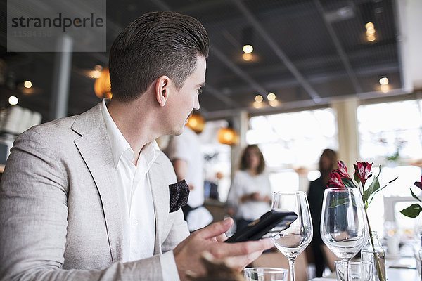 Geschäftsmann schaut weg  während er sein Handy im Restaurant hält.