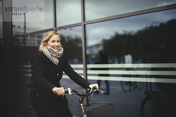 Lächelnde mittlere erwachsene Geschäftsfrau auf dem Fahrrad beim Stadtbau