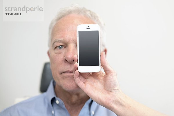 Älterer Mann mit Smartphone vor dem Auge.