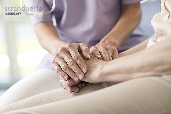 Eine Pflegekraft hält die Hände einer älteren Frau.