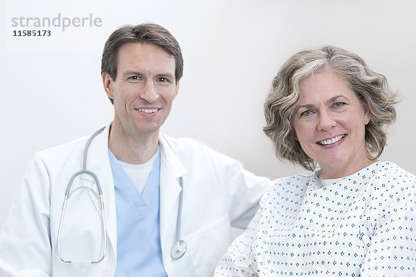 Männlicher Arzt und weibliche Patientin lächeln in Richtung Kamera.