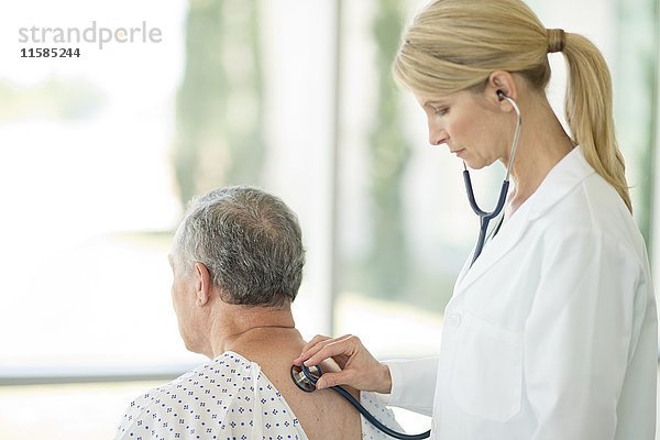 Eine Ärztin benutzt ein Stethoskop bei einem männlichen Patienten.