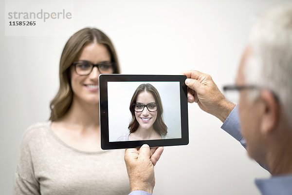 Mann hält digitales Tablet vor das Gesicht einer Frau.