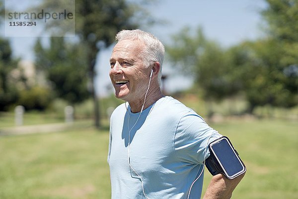 Älterer Mann mit Smartphone am Arm und Kopfhörern im Park.