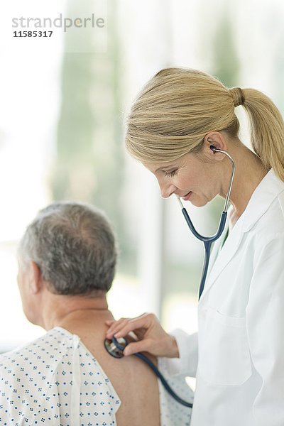 Eine Ärztin benutzt ein Stethoskop bei einem männlichen Patienten.