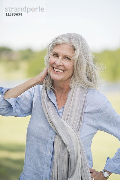 Ältere Frau mit grauem Haar und Kopftuch im Freien  lächelnd.