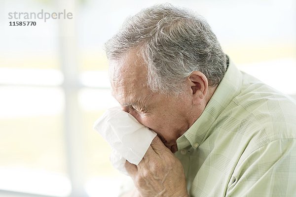 Ein älterer Mann putzt sich die Nase mit einem Taschentuch.