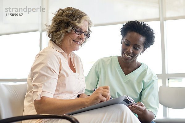 Ältere Frau füllt mit einer Krankenschwester ein Formular aus und lächelt.