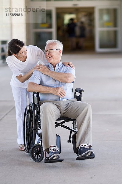 Älterer Mann im Rollstuhl mit Pflegekraft.