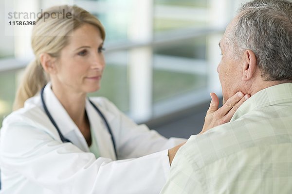 Eine Ärztin berührt den Hals eines älteren Mannes.