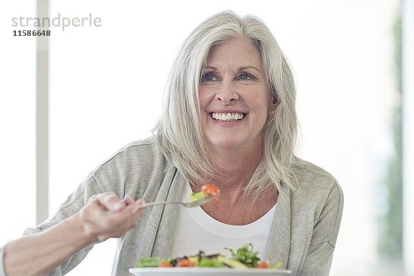 Ältere Frau isst Salat und lächelt.