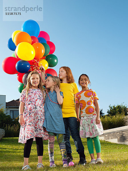 Mädchen stehen auf dem Rasen und halten mehrfarbige Luftballons.