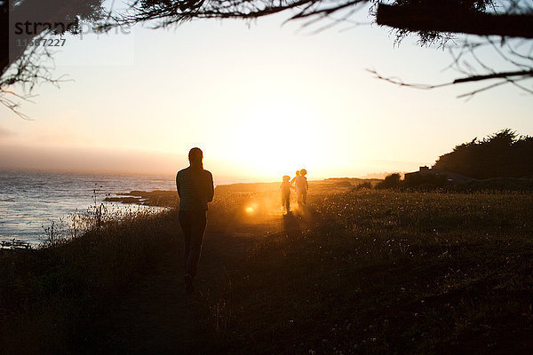 Familie geht bei Sonnenuntergang an der Küste entlang