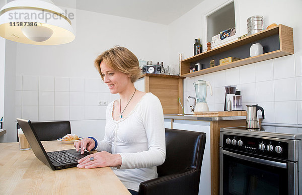 Frau mit Laptop und Snack in der Küche