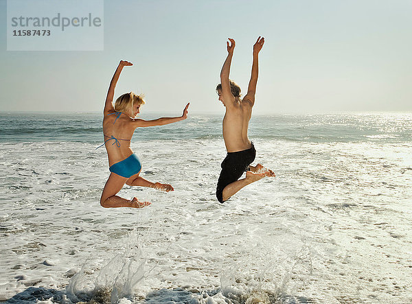 Paar springt am Strand in Wellen