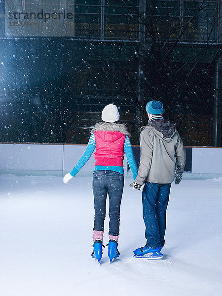 Paar hält sich auf der Eisbahn an den Händen und beobachtet den Schneefall