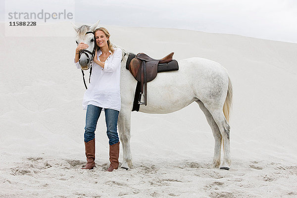 Blonde Frau mit Pferd am Strand