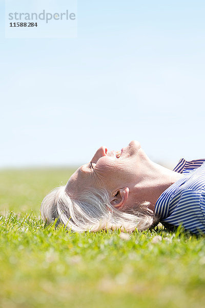 Reife Frau liegt lächelnd im Gras