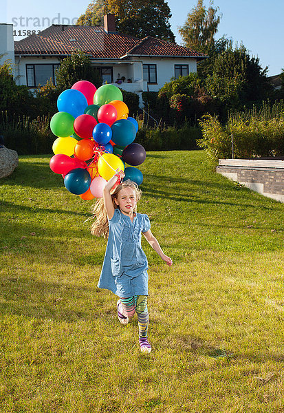 Mädchen läuft mit bunten Luftballons über den Rasen