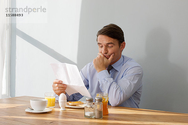 Mann am Frühstückstisch  der einen Brief liest