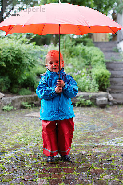 Kleinkind mit Regenschirm im Hinterhof