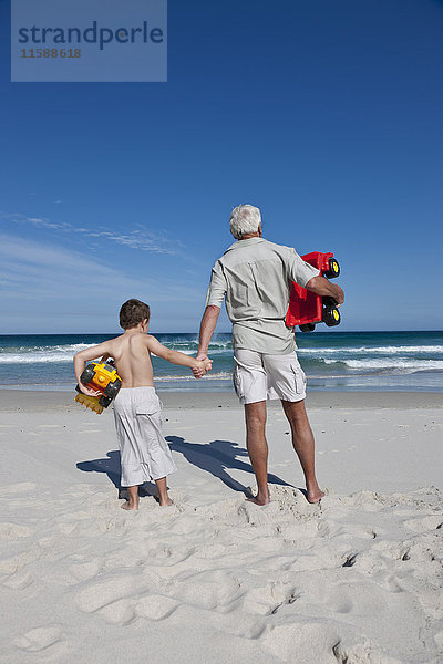 Mann hält die Hand seines Enkels am Strand