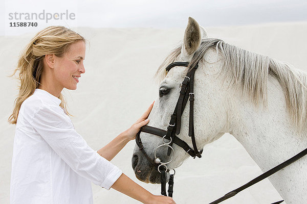 Blonde Frau mit Pferd am Strand