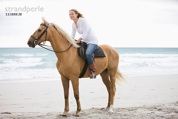 Frau reitet auf einem Pferd am Strand