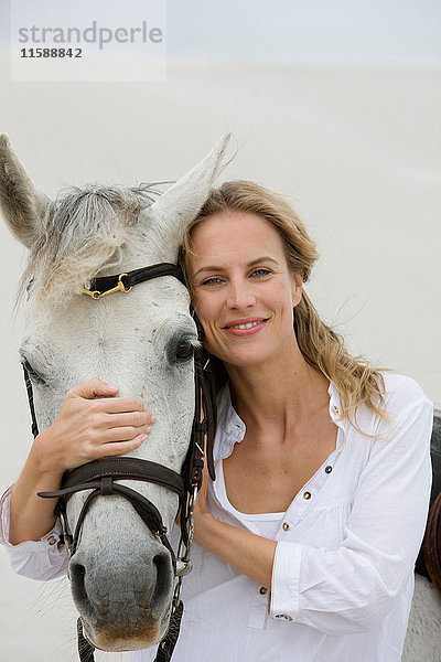 Blonde Frau mit Pferd am Strand