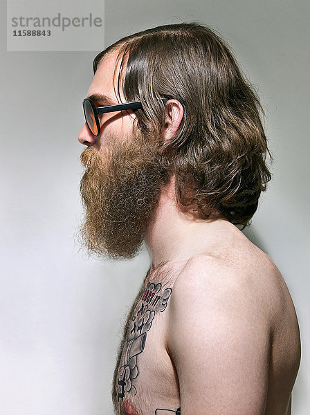 Junger Mann mit Bart und Tätowierungen auf der Brust  Seitenansicht