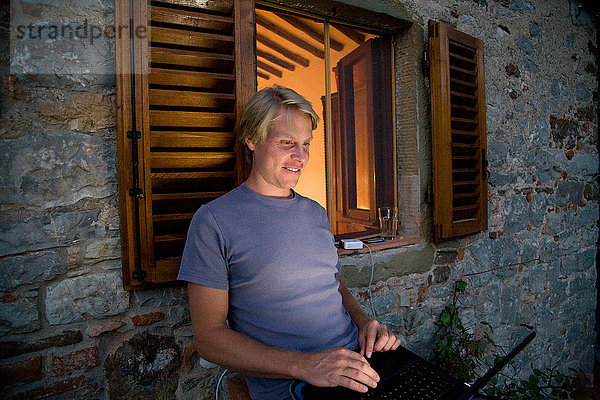 Mann mit Laptop außen beleuchtetes Fenster
