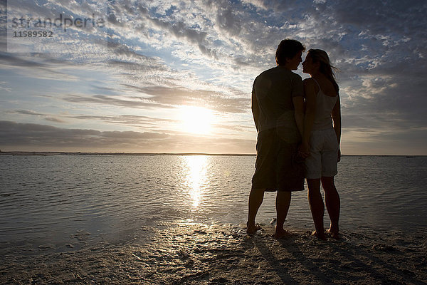 Ein Paar küsst sich bei Sonnenuntergang am Strand