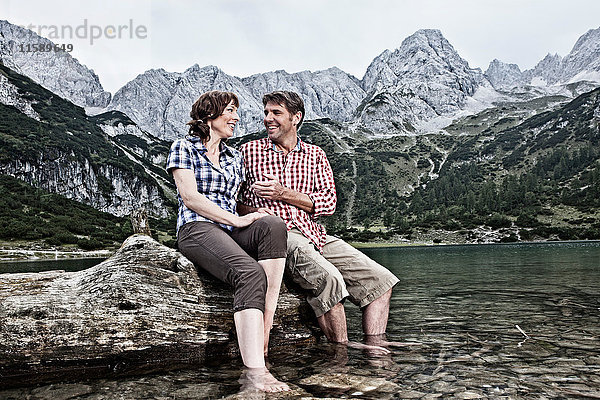 Lächelndes Paar mit baumelnden Füßen im See