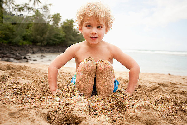 Junge mit im Sand begrabenen Füßen am Strand  Porträt