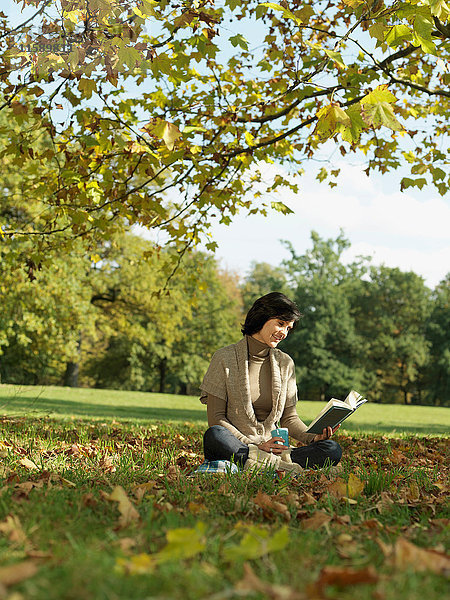 Frau unter dem Baum liest Buch im Herbst