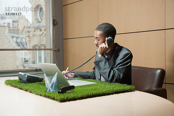 Mann telefoniert an grasbedecktem Schreibtisch