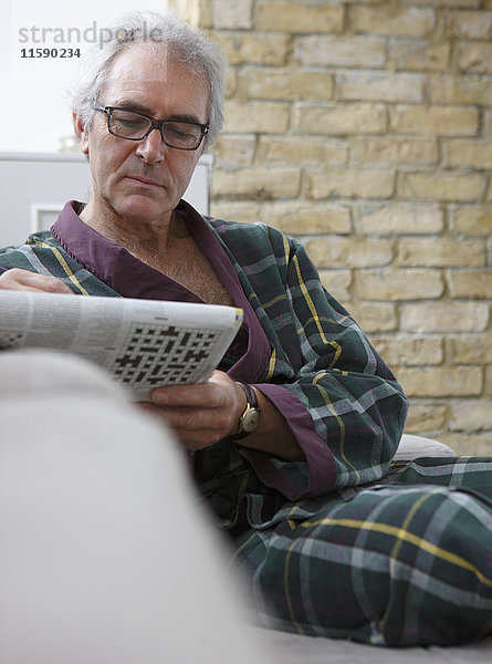 Älterer Mann in entspannendem Gewand mit Zeitung