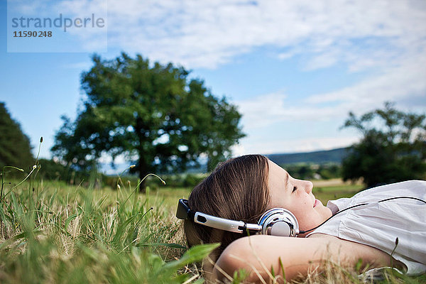 Mädchen mit Kopfhörern im Gras liegend