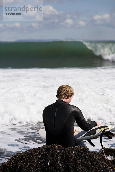 Surfer  der in Wellen auf Seegras sitzt