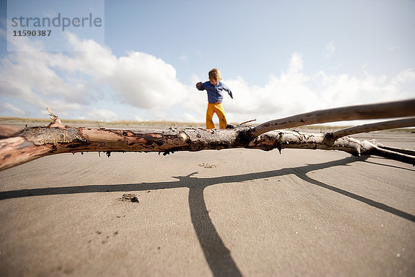 Junge spielt am Sandstrand mit Treibholz