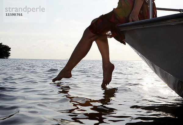 Ältere Frau sitzt auf der Kante eines Motorbootes mit den Füßen im Wasser