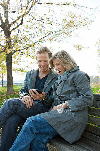 Mutter und erwachsener Sohn auf Parkbank mit Blick auf Smartphone