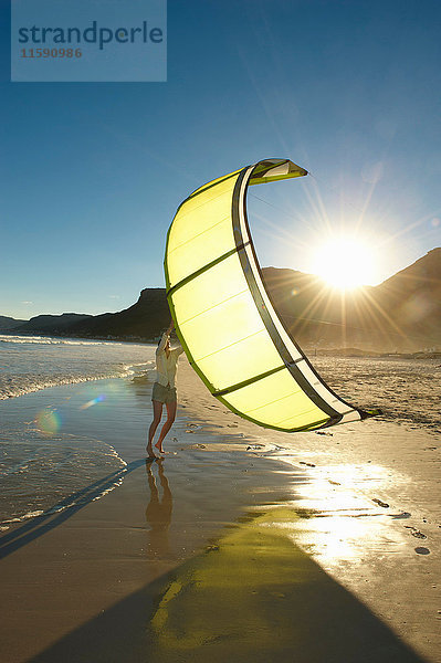 Frau hält Kitesurfing-Segel am Strand.