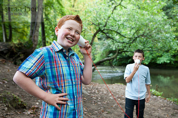 Zwei Jungen benutzen Pappbecher und Schnur zur Kommunikation im Wald