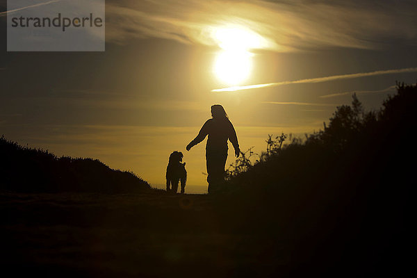 Frau geht bei Sonnenuntergang mit ihrem Hund spazieren