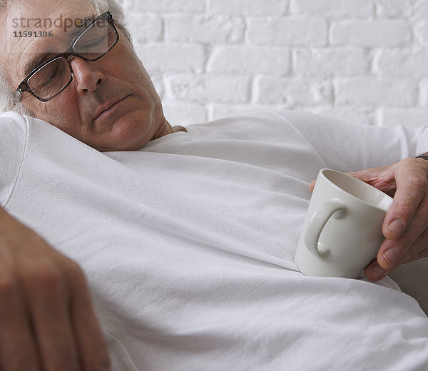 Senior Mann schläft und hält Kaffeetasse