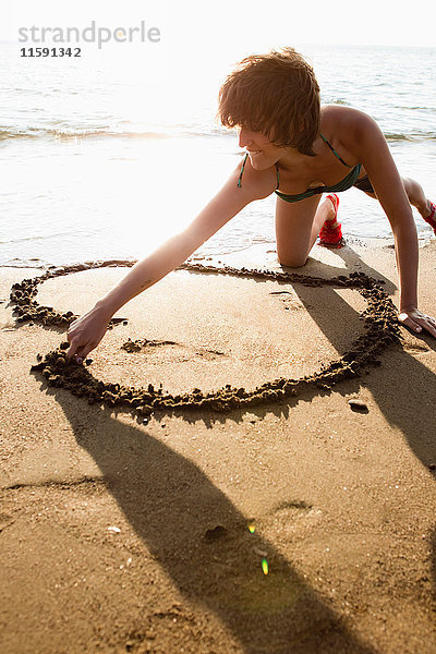 Frau malt Herz im Sand am Strand