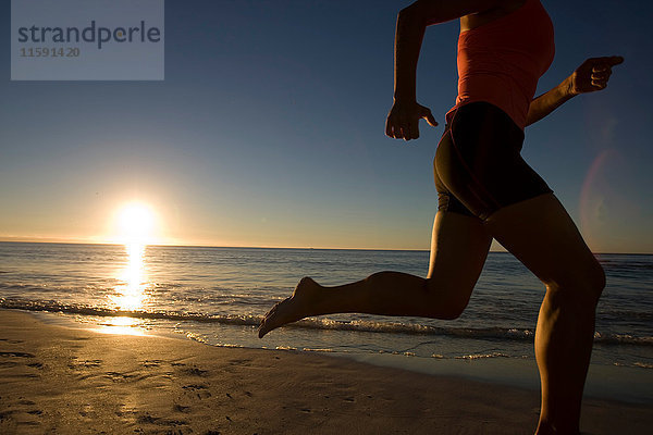 Junge Frau rennt bei Sonnenuntergang am Strand